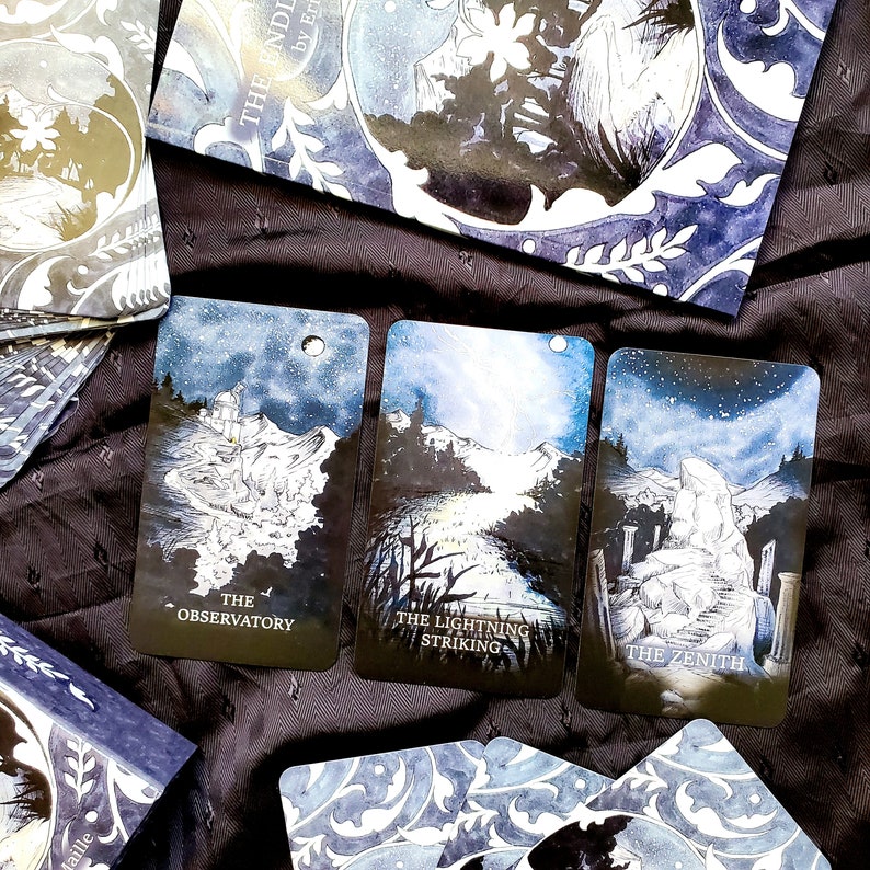 May include: A deck of tarot cards with a celestial theme. Three cards are visible, each featuring a different landscape scene with text: "The Observatory", "The Lightning Striking", and "The Zenith". The cards have a blue and white color scheme, with a starry night sky.