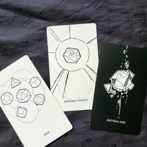 Puede incluir: Tres cartas con ilustraciones geom&eacute;tricas de dados. Una carta dice "DICE", otra "NATURAL TWENTY" y la tercera "NATURAL ONE". Las cartas son blancas con dibujos lineales negros y una carta negra con dibujos lineales blancos.