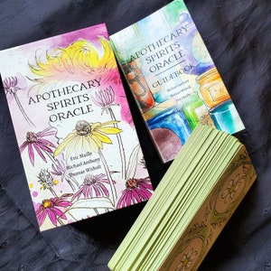 K&ouml;nnte beinhalten: Ein Deck Apothecary Spirits Oracle-Karten mit einem Handbuch. Die Karten zeigen ein gr&uuml;nes und goldenes Design mit einem floralen Motiv. Das Handbuch hat eine Aquarell-Illustration von Gl&auml;sern und Flaschen mit einem floralen Motiv.