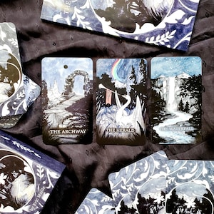May include: A deck of tarot cards with a celestial theme. The cards feature illustrations of an archway, a swan with a rainbow, and a waterfall. The cards are in shades of blue and white, with the titles "The Archway", "The Herald", and "The Waterfall".