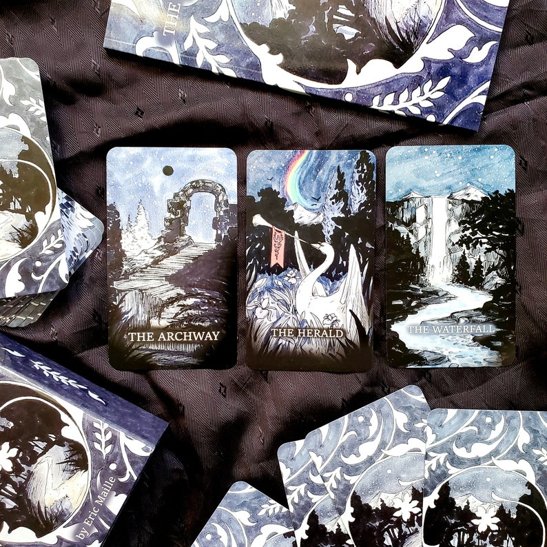 May include: A deck of tarot cards with a celestial theme. The cards feature illustrations of an archway, a swan with a rainbow, and a waterfall. The cards are in shades of blue and white, with the titles "The Archway", "The Herald", and "The Waterfall".