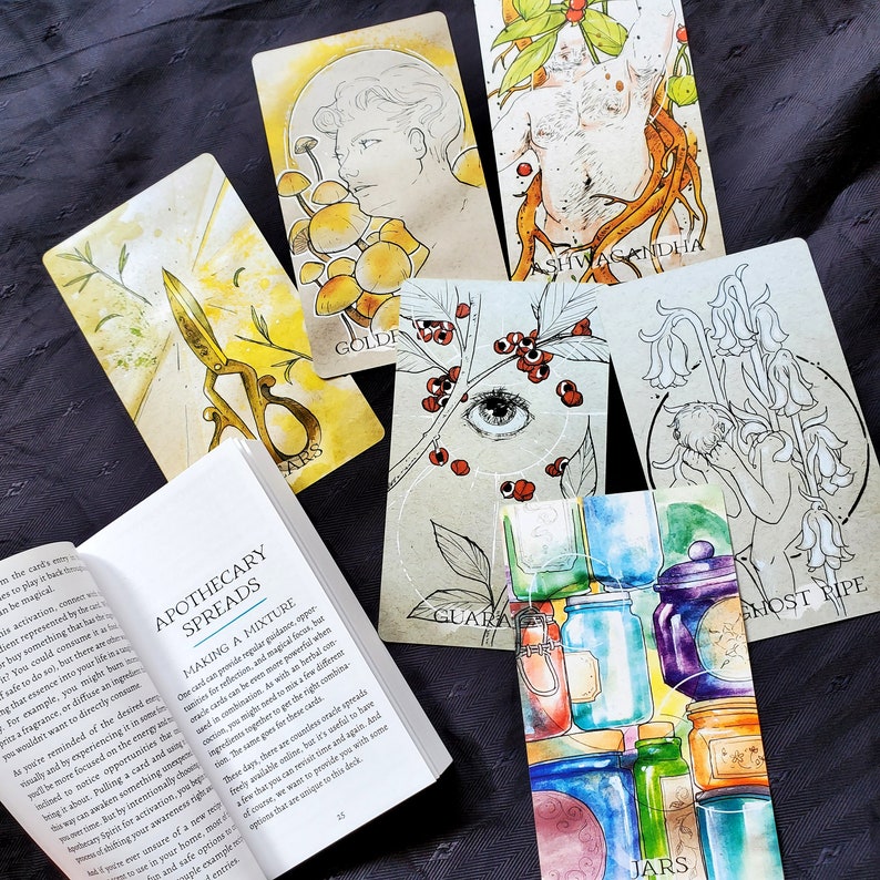 K&ouml;nnte beinhalten: Eine Sammlung von Tarotkarten mit Illustrationen von Blumen, Beeren und einer Person. Die Karten liegen auf einer dunkelgrauen Stoffoberfl&auml;che. Der Text auf den Karten lautet "Gold", "Ashwagandha", "Most Ripe", "Guara" und "Jars".