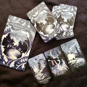 May include: An oracle deck and guidebook titled "The Endless Oracle" by Eric Maille. The deck features illustrated cards with scenes like "The Archway," "The Herald," and "The Figure by the Fire." The book and cards have a dark blue and white color scheme.