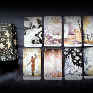 Pu&ograve; includere: Una scatola di mazzo di tarocchi con il titolo "The Ink Witch Tarot Deck, Second Edition" di Eric Maille. La scatola &egrave; nera con un design floreale dorato. Le carte dei tarocchi sono disposte su una superficie scura. Le carte presentano illustrazioni di spade, coppe, bastoni e pentacoli.