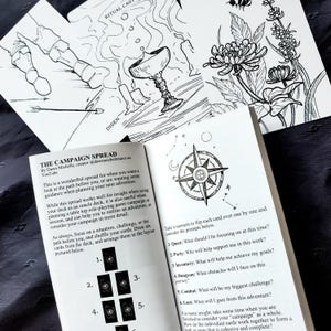 Puede incluir: Un libro abierto con una ilustraci&oacute;n de rosa de los vientos y texto, junto con dos cartas ilustradas en blanco y negro. Una carta presenta un mapa, la otra flores. El t&iacute;tulo del libro es "THE CAMPAIGN SPREAD".