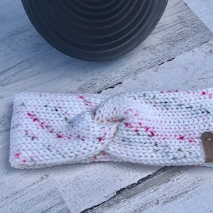 May include: White knitted headband with a pink and gray speckled pattern and a brown leather accent.