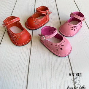 May include: Three pairs of doll shoes in red and pink leather with a flower cut-out design. The shoes have a strap with a buckle closure.  ANDREJ shoes for dolls.