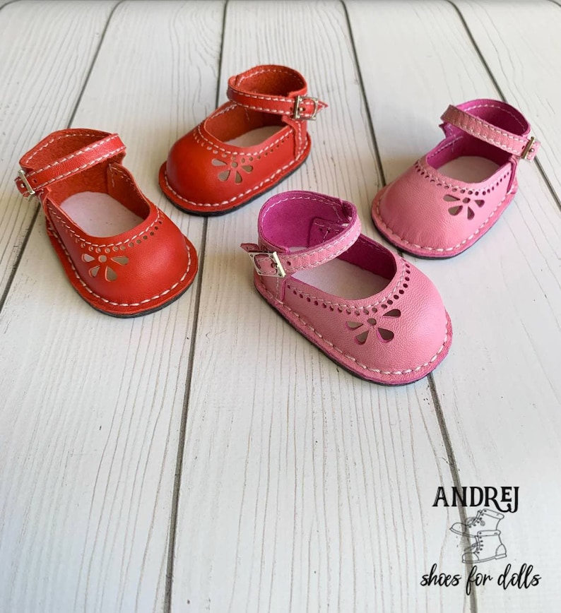 May include: Three pairs of doll shoes in red and pink leather with a flower cut-out design. The shoes have a strap with a buckle closure.  ANDREJ shoes for dolls.