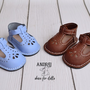 May include: Two pairs of doll shoes, one pair is light blue and the other is brown. Both pairs have a strap with a buckle and are made of leather. The shoes have a decorative cut-out design.