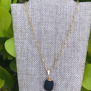 May include: A gold chain necklace with a black stone pendant. The pendant is a rough, irregular shape and has a gold bail.