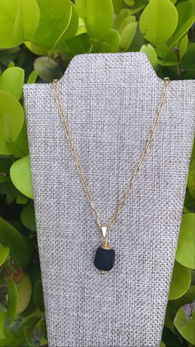May include: A gold chain necklace with a black stone pendant. The pendant is a rough, irregular shape and has a gold bail.