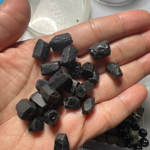 Puede incluir: Una mano sosteniendo un mont&oacute;n de piedras negras, &aacute;speras y de forma irregular. Las piedras parecen ser piedras preciosas o cristales.