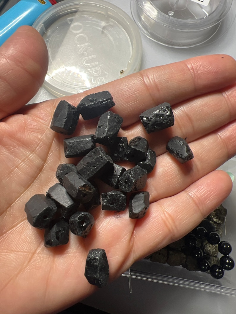 Puede incluir: Una mano sosteniendo un mont&oacute;n de piedras negras, &aacute;speras y de forma irregular. Las piedras parecen ser piedras preciosas o cristales.