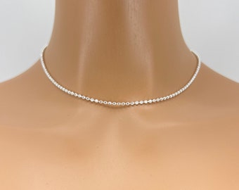 May include: A silver beaded choker necklace on a mannequin. The necklace is thin and delicate, with small, round beads.
