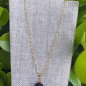 May include: A gold chain necklace with a black pendant and red beads. The pendant is a smooth, rounded shape.