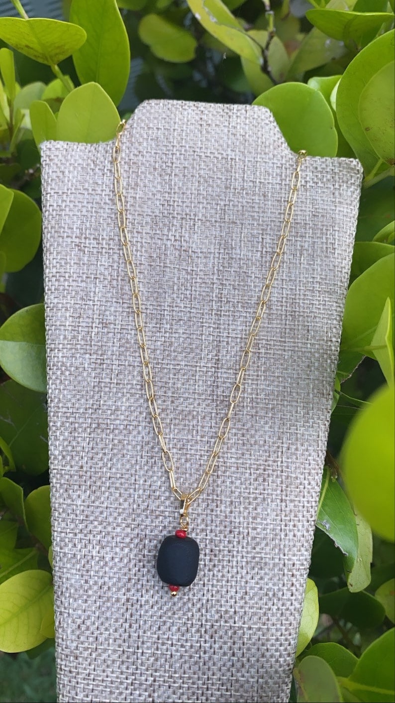 May include: A gold chain necklace with a black pendant and red beads. The pendant is a smooth, rounded shape.