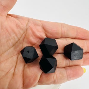 May include: Four black wooden geometric beads with a hole in the centre. The beads are in the shape of a diamond with multiple facets.