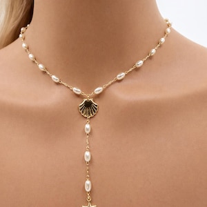 May include: Gold-toned necklace featuring a seashell pendant and a dangling strand of pearls. The necklace has a delicate chain with small pearls and a starfish charm at the end of the strand. A stylish piece of jewelry.