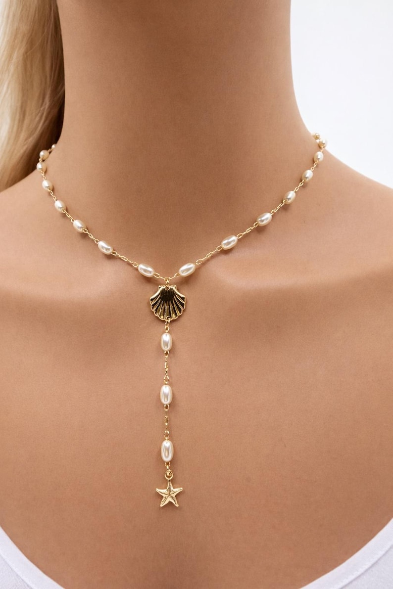 May include: Gold-toned necklace featuring a seashell pendant and a dangling strand of pearls. The necklace has a delicate chain with small pearls and a starfish charm at the end of the strand. A stylish piece of jewelry.
