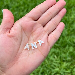 May include: A white pearl necklace with the name "ANA" spelled out in white pearl letters.