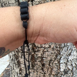 May include: A black bracelet with cylindrical beads and a black cord with adjustable length.