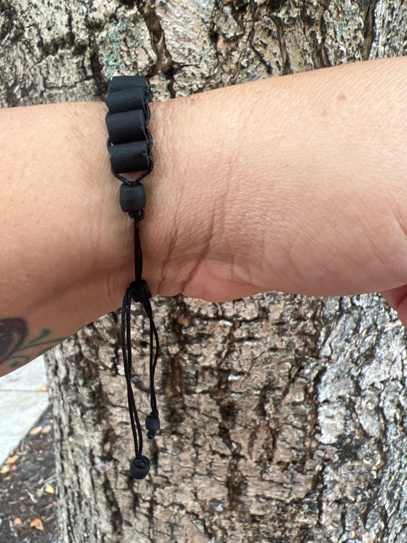 May include: A black bracelet with cylindrical beads and a black cord with adjustable length.