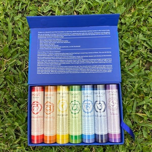 Op de afbeelding: Een set van zeven chakra-kaarsen in een blauwe doos. De kaarsen zijn gelabeld met de namen van de chakra's: Wortel, Sacraal, Zonnevlecht, Hart, Keel, Derde Oog en Kroon. Elke kaars is een andere kleur van de regenboog, beginnend met rood en eindigend met violet.
