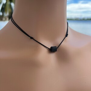 Puede incluir: Un collar negro simple con un peque&ntilde;o colgante rectangular negro.