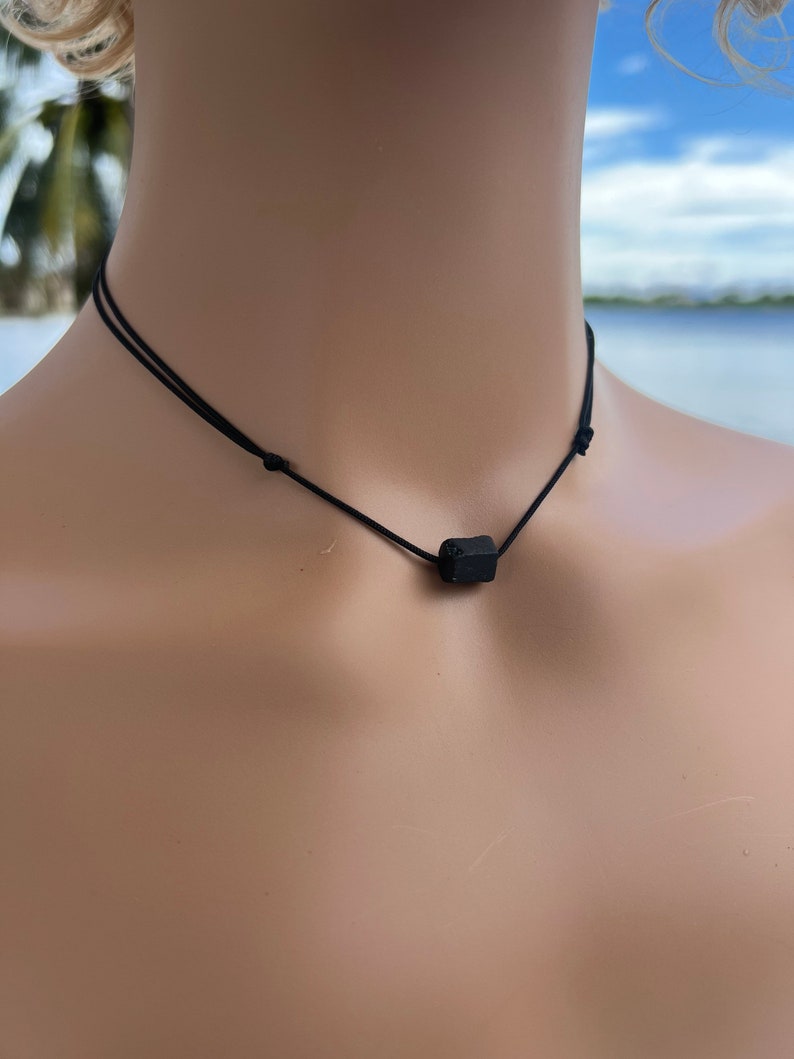Puede incluir: Un collar negro simple con un peque&ntilde;o colgante rectangular negro.