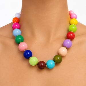 May include: A multi-colored beaded necklace featuring large, smooth, spherical beads in a variety of vibrant hues including pink, yellow, green, red, purple, blue, orange, and brown, separated by small gold-toned metallic spacer beads.