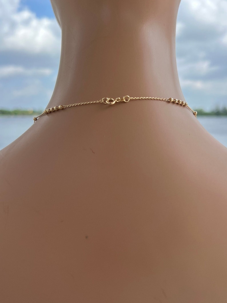 Puede incluir: Un collar de cadena de oro con un delicado dise&ntilde;o de cuentas. La cadena se muestra en el cuello de un maniqu&iacute;.