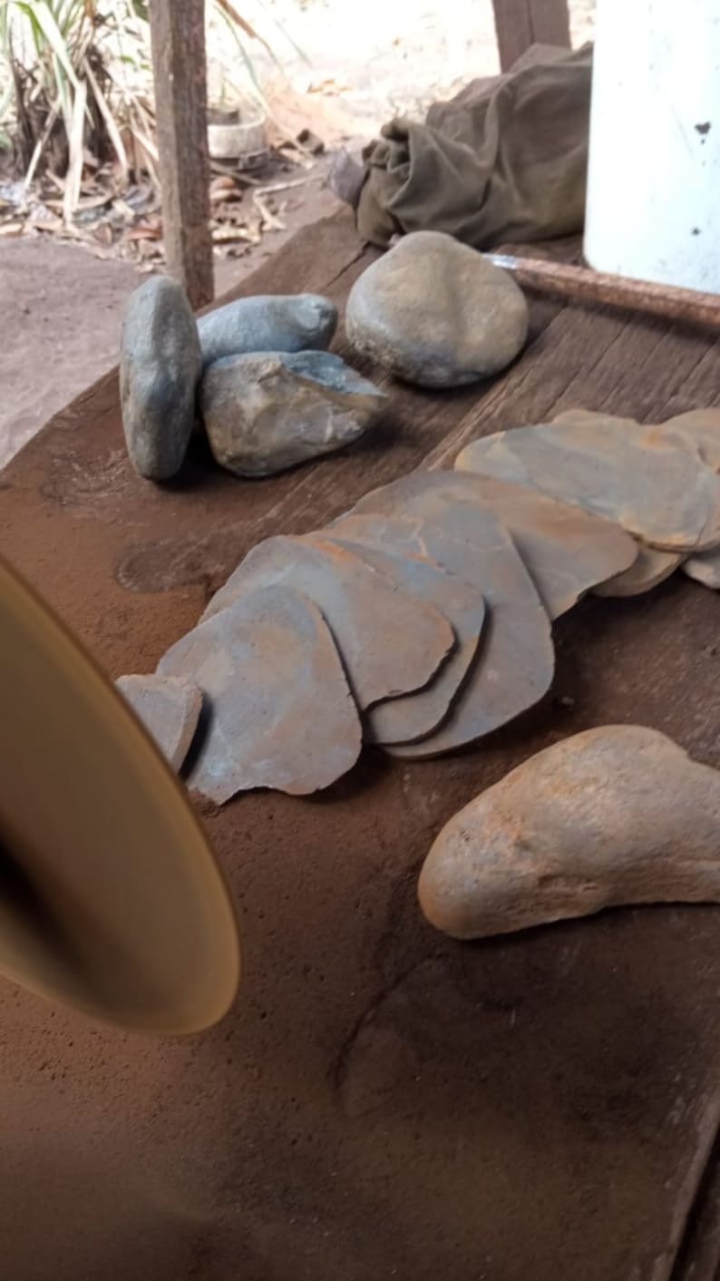 May include: A close-up of a pile of smooth, gray-brown stones, some of which are stacked on top of each other. The stones are on a wooden surface, and there is a metal disc in the foreground.