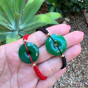May include: Two jade bracelets with green jade round pendants and red and black string cords.
