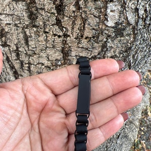 May include: A black bracelet with a rectangular black plate. The bracelet is made of small black beads.