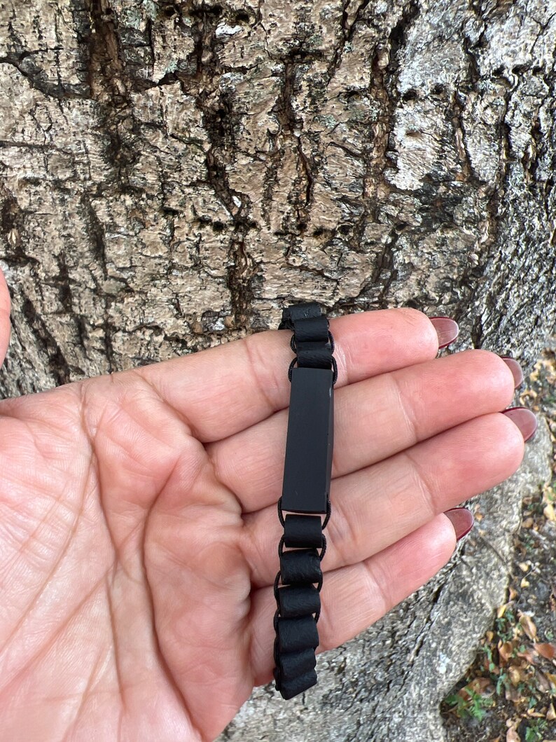 May include: A black bracelet with a rectangular black plate. The bracelet is made of small black beads.