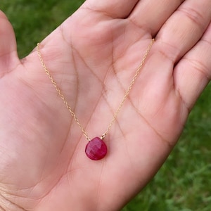 Könnte beinhalten: Eine zarte goldene Kettenkette mit einem einzelnen tropfenförmigen roten Edelstein-Anhänger.