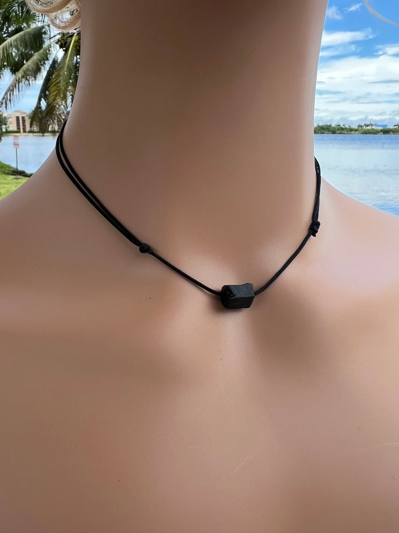 Puede incluir: Un collar de piedra de lava negra con un cord&oacute;n negro. El collar est&aacute; en el cuello de un maniqu&iacute;.