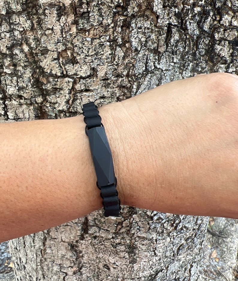May include: A black silicone bracelet with a geometric black charm. The bracelet is adjustable and has a simple design.