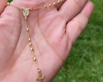 May include: A gold-toned rosary necklace with a small cross charm and a pendant featuring the Virgin Mary.