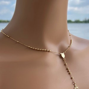Puede incluir: Un collar de rosario dorado con un peque&ntilde;o dije de cruz. El collar est&aacute; hecho de peque&ntilde;as cuentas redondas y tiene un colgante con una imagen religiosa.