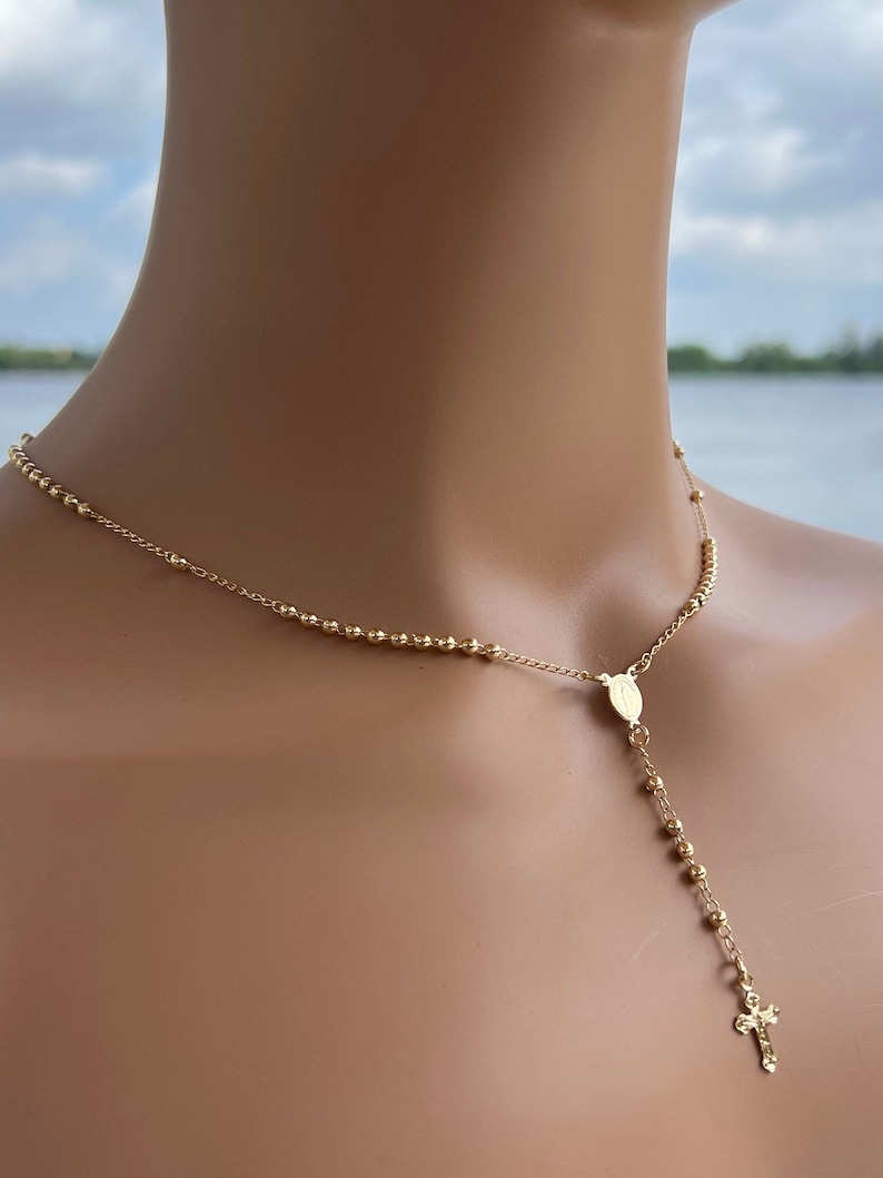Puede incluir: Un collar de rosario dorado con un peque&ntilde;o dije de cruz. El collar est&aacute; hecho de peque&ntilde;as cuentas redondas y tiene un colgante con una imagen religiosa.