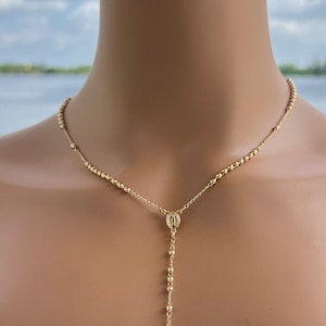 Puede incluir: Un collar de rosario dorado con un peque&ntilde;o dije de cruz y un dije redondo.
