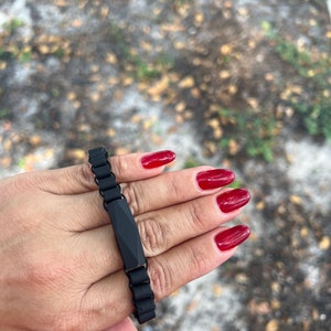 May include: A black bracelet with a rectangular, faceted charm. The bracelet is made of a chain-like material.