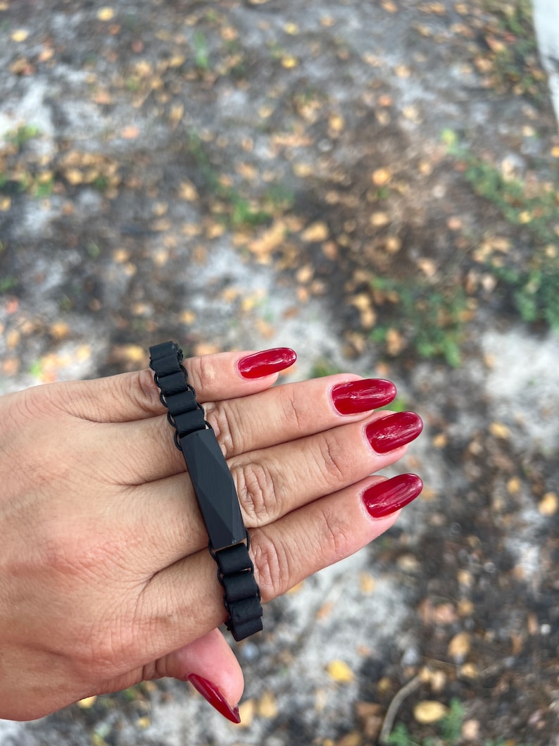 May include: A black bracelet with a rectangular, faceted charm. The bracelet is made of a chain-like material.