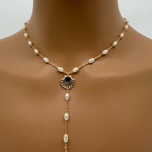 May include: Gold-toned necklace featuring a seashell pendant with dangling pearls and a starfish charm. The necklace is adorned with small, oval-shaped pearls along the chain, creating a delicate and elegant design.