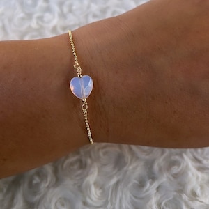May include: A delicate gold chain bracelet with a single heart-shaped opal charm.