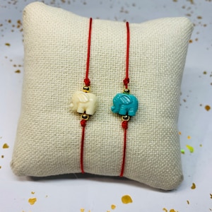 May include: Two red string bracelets with gold beads and elephant charms. One charm is white and the other is turquoise.
