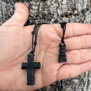 Könnte beinhalten: Zwei schwarze Holzketten mit einem Kreuz- und einem Handanhänger an schwarzen Schnüren.