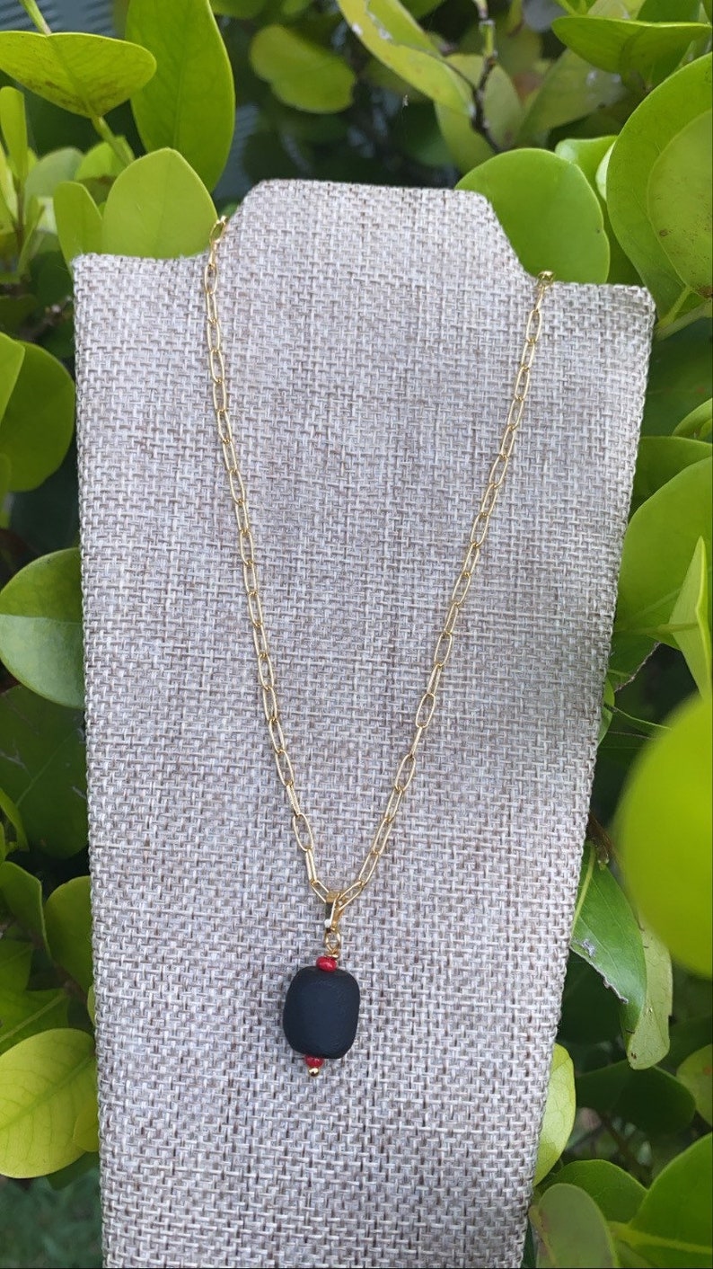 May include: A gold chain necklace with a black pendant and red beads. The pendant is a smooth, rounded shape.