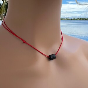Puede incluir: Un collar sencillo con un colgante de piedra negra en un cord&oacute;n rojo.